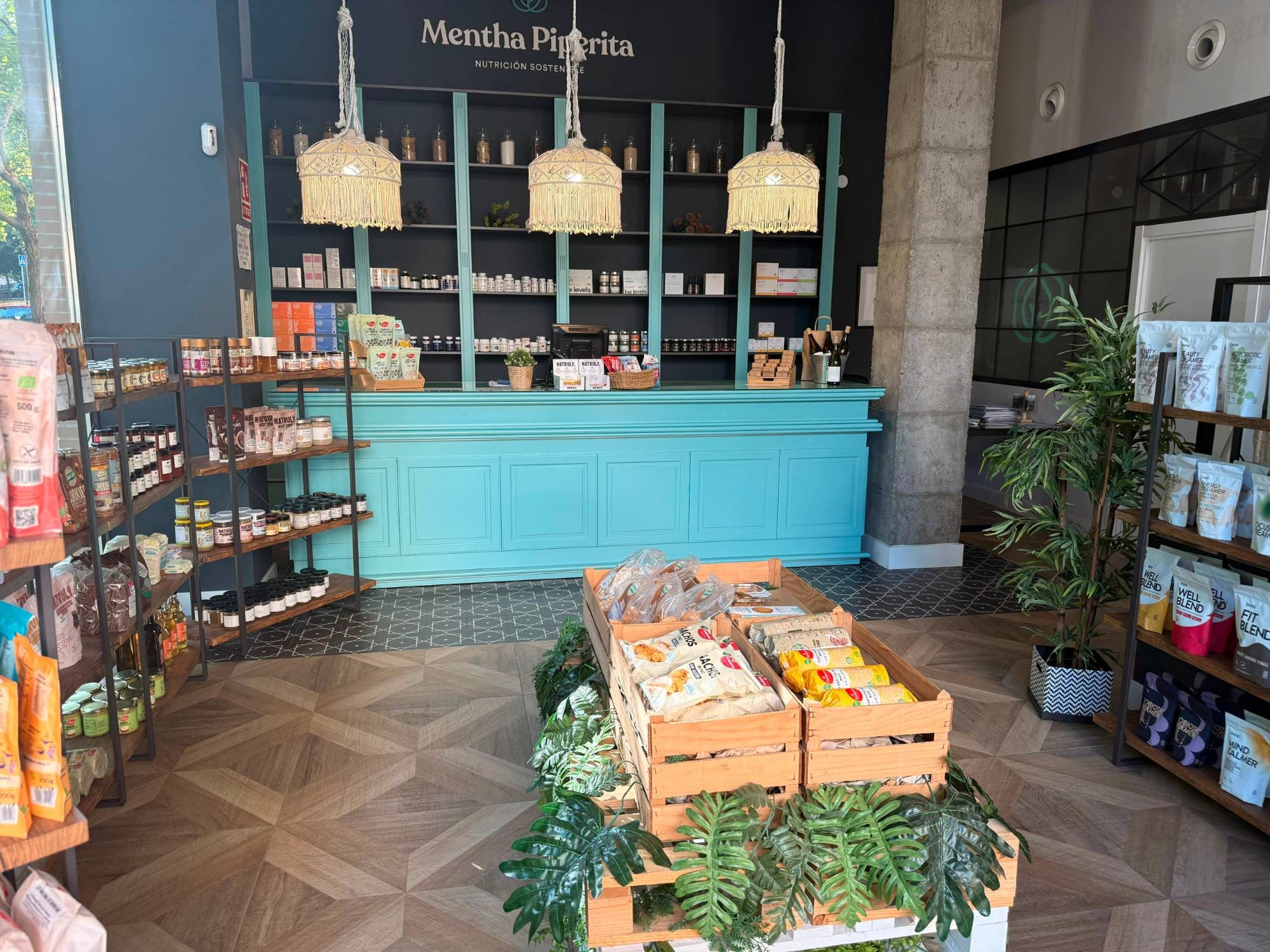 Interior de la tienda de Mentha Piperita en Badajoz: mostrador turquesa, lámparas de macramé, estanterías con complementos y cajas de madera con productos ecológicos