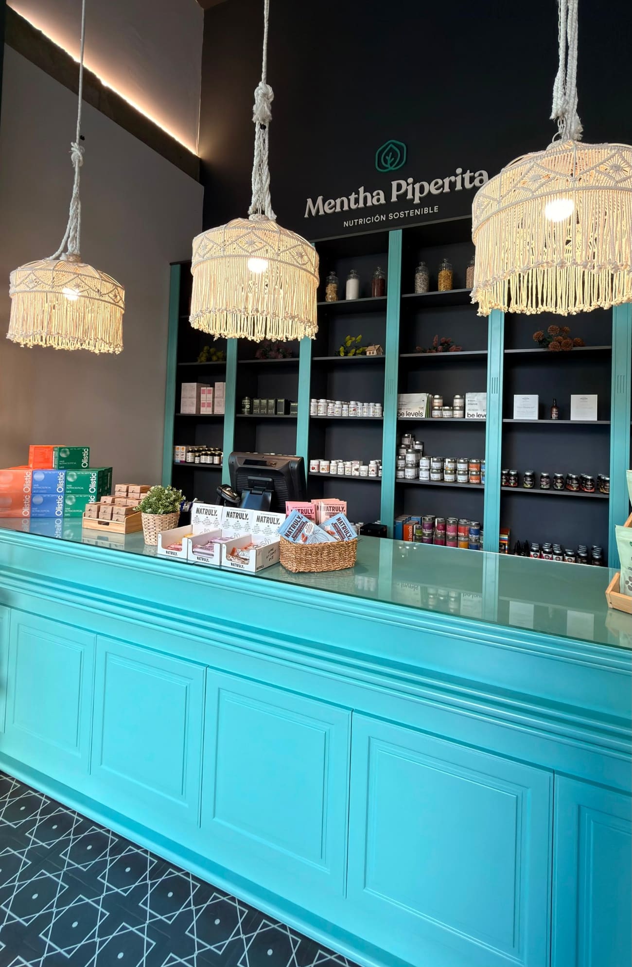 Mostrador turquesa de Mentha Piperita con lámparas de macramé; al fondo, el rótulo de la marca